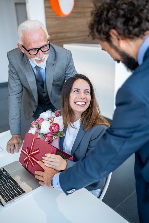 Business team celebrating a special occasion by giving a female colleague a beautiful bouquet and heartfelt gifts in the office, expressing appreciation and joy for her achievement